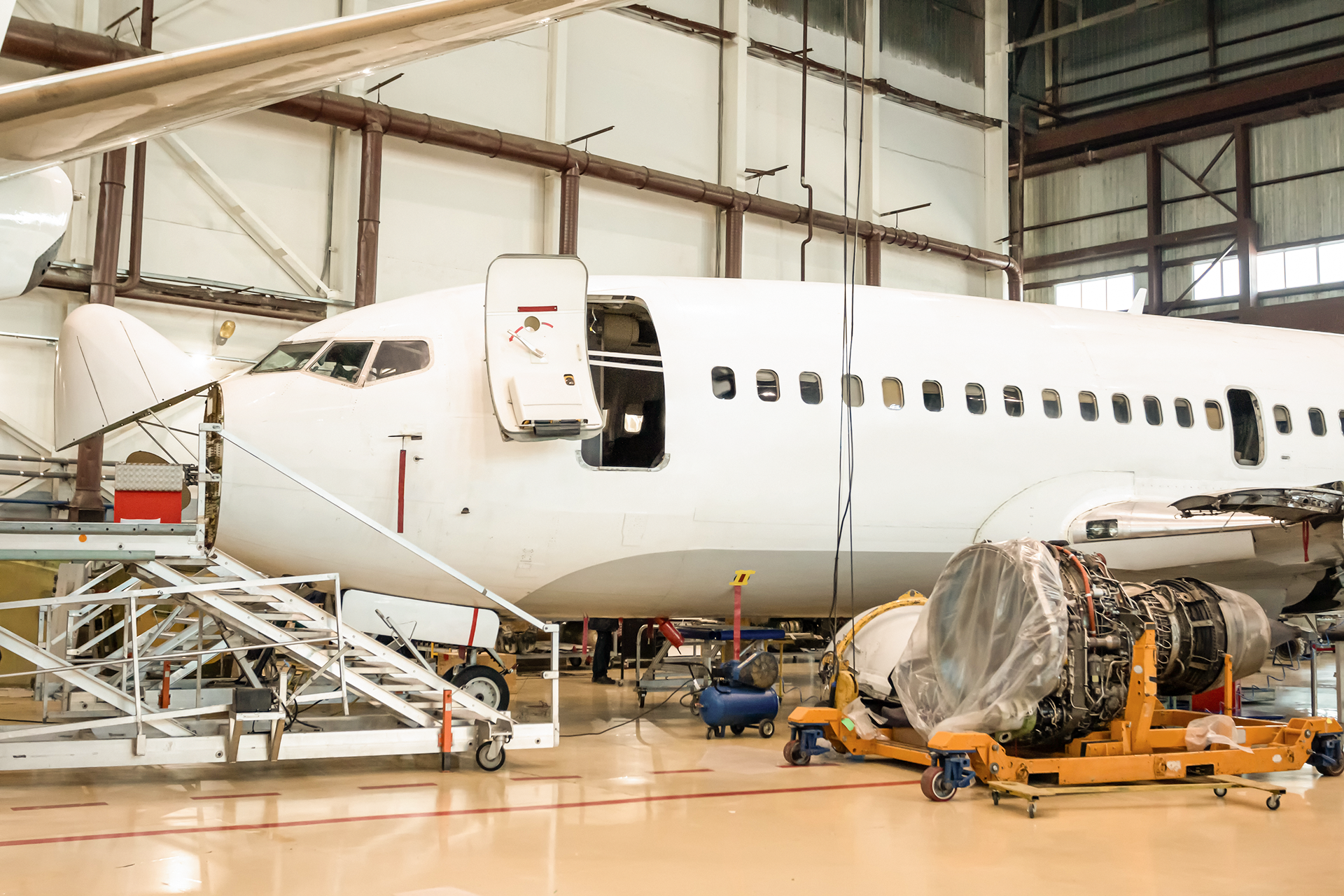 Aircraft undergoing maintenance inside MRO hangar with tools and repair equipme